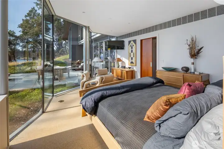 Comfortable guest suite with walls of glass opening to tranquil garden and waterfront views, providing a peaceful retreat for visitors.