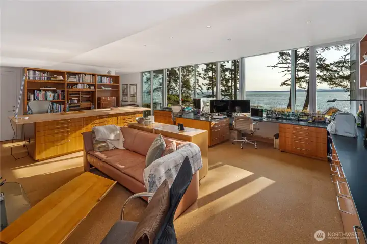 Spectacular light-filled workspace with custom cabinetry, multiple workstations, and an entire wall of windows framing breathtaking water views—an inspiring setting for work, creativity, or study.