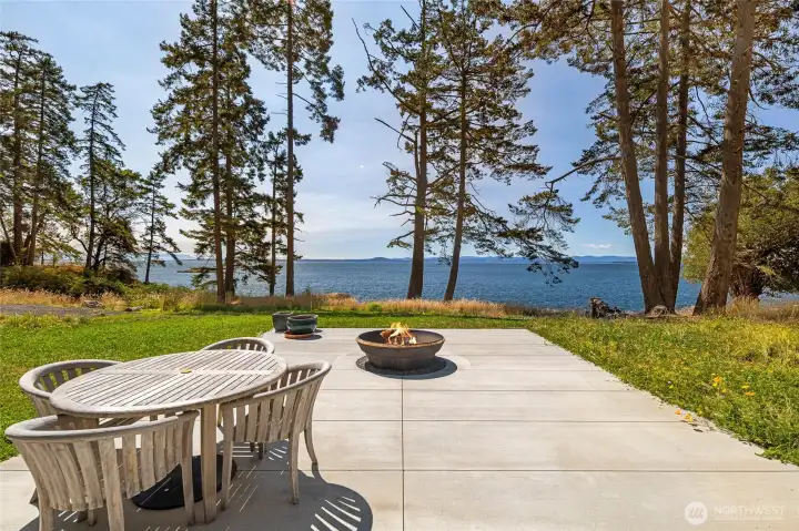 Entertain or unwind on the expansive waterfront patio featuring a firepit and outdoor dining space, perfectly positioned to take in sweeping views across the water and surrounding islands.