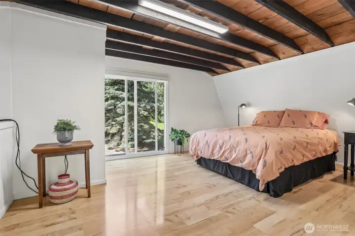Exposed wood beams and expansive windows create a warm and inviting primary bedroom with views of the surrounding landscape.