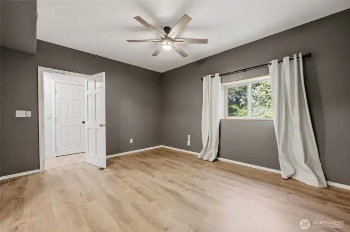 Past the kitchen is this spacious room with ceiling fan; closet door seen ahead, with exterior access door further down to the right.