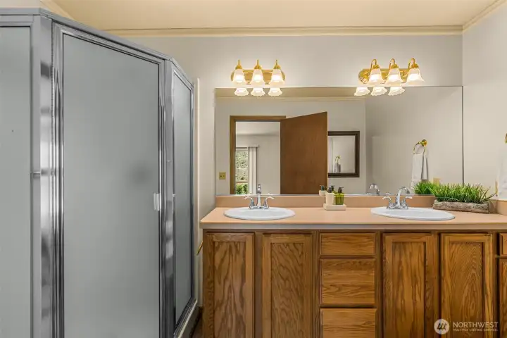 Enjoy the convenience of this highly functional primary en-suite bathroom. Designed for easy everyday living, the space features a sprawling vanity with dual sinks, plenty of warm wood cabinetry for all your storage needs, and a large walk-in shower.