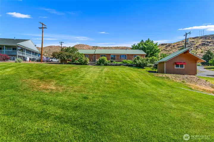 Look at all that space! Looking up from the lower yard, this view highlights the sprawling, meticulously maintained green lawn, the expansive back deck, and the versatile she shed. A true Pateros oasis!