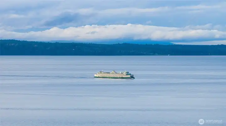 A stunning view of the Edmonds-Kingston ferry making its way across Puget Sound, captured from the waterfront with sparkling water and surrounding scenery.