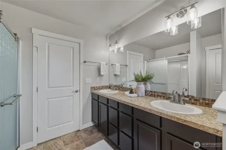 Dual vanity in the primary bathroom with a linen closet and walk in shower.