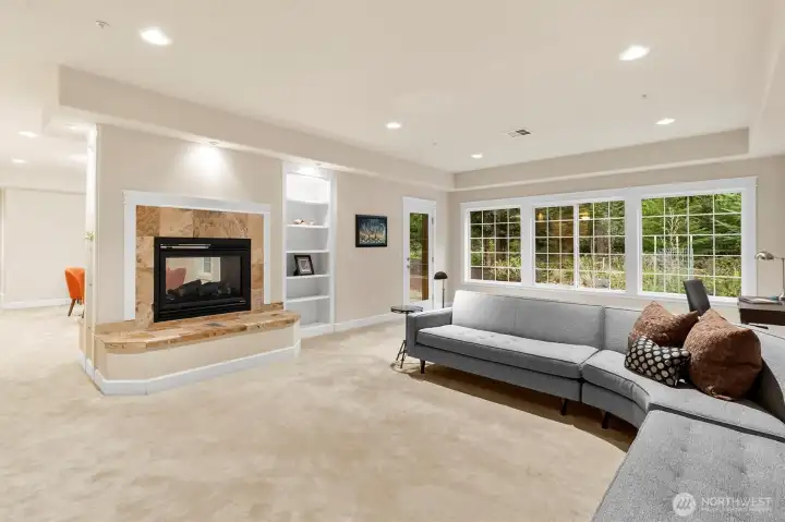 Light-filled living room featuring a wall of windows overlooking the forest, custom built-ins, and a gas fireplace, with direct access to the covered patio for seamless indoor-outdoor living.
