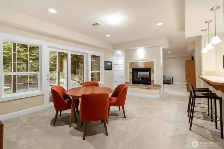 Dining area with views of the forest, featuring the opposite side of the double-sided gas fireplace. This area also has custom built-ins, with sliding door access to the covered patio and an open flow to the kitchen with bar seating.