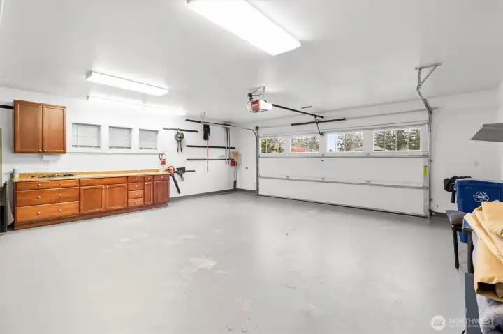 Spacious two-car garage featuring a durable finished floor, built-in counter workspace, and ample storage with cabinets and drawers, ideal for organization, hobbies, or projects.