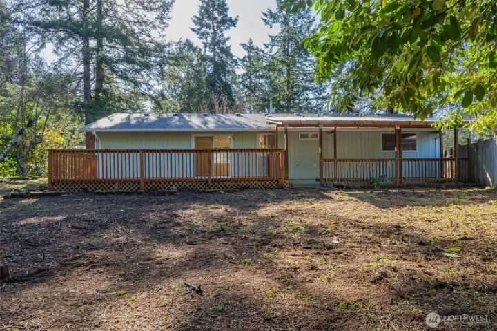 Very private, partially fenced backyard looking back at the home. You can see the deck and covered patio.