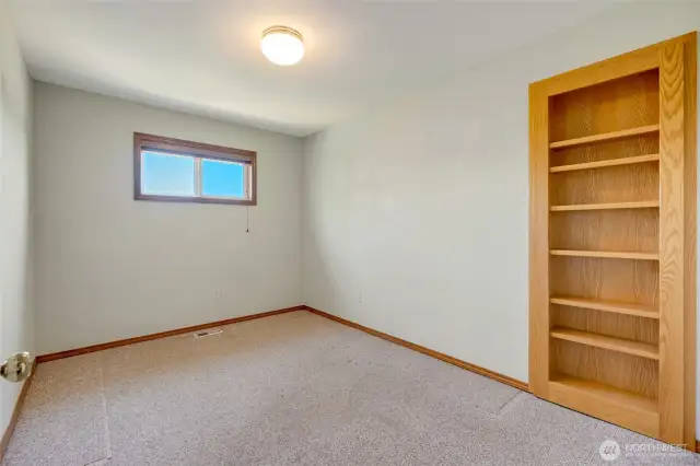 Versatile room off garage with hidden closet behind built-in shelves.