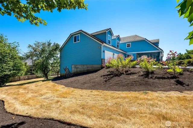 Side yard with fresh landscaping, offering a gentle slope and room for additional garden or outdoor features.
