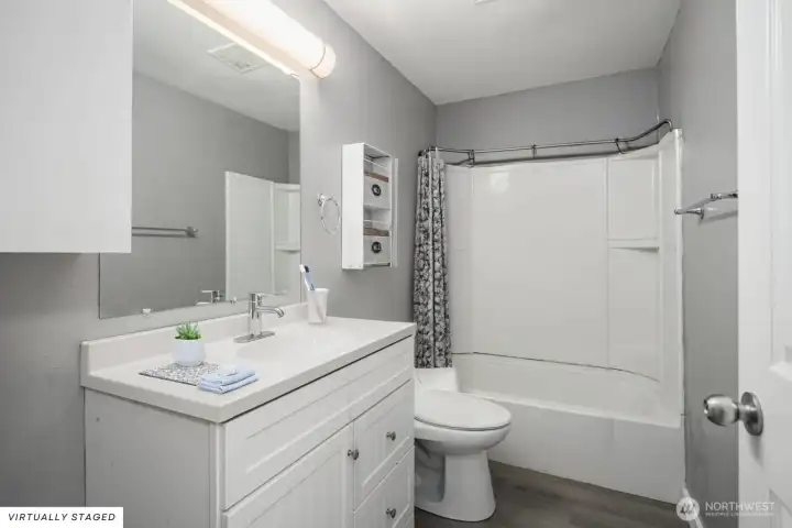 Clean and updated bathroom with modern vanity, large mirror, and a combination tub/shower with built-in shelving.