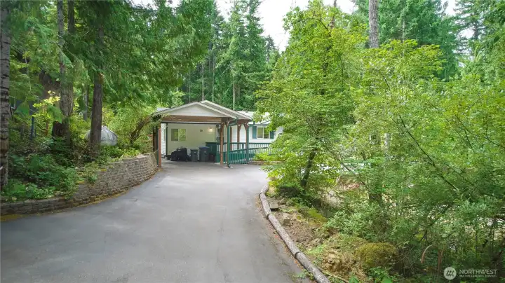 A welcoming, paved driveway leads to a spacious covered carport, nestled within a serene, beautifully wooded setting that offers exceptional privacy and Northwest charm.