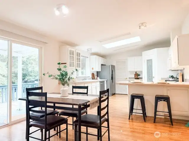 A bright, open-concept dining area featuring beautiful hardwood floors, seamless flow into the kitchen, and a sliding glass door that leads out to the spacious back deck.
