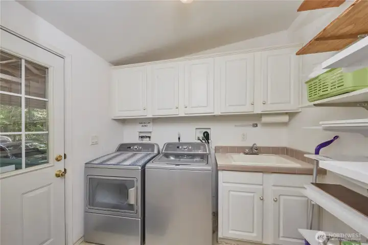 This highly functional, dedicated laundry room comes complete with modern stainless steel front-load appliances, overhead storage cabinets, a built-in utility sink, and a separate exterior door for easy backyard access.