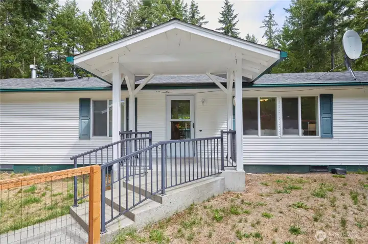 The inviting front entry (which is on opposite side of driveway) features a concrete staircase with sturdy safety railings, a covered porch, and classic decorative shutters