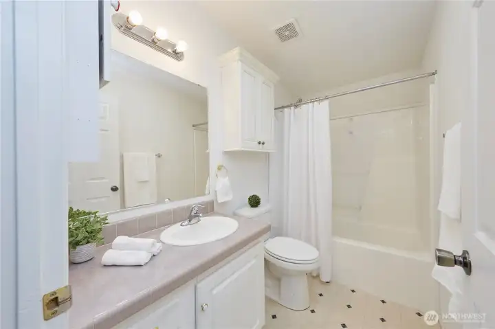 A clean and bright full bathroom featuring a generous vanity, ample cabinet storage, a large mirror, and a classic tub-and-shower combo.