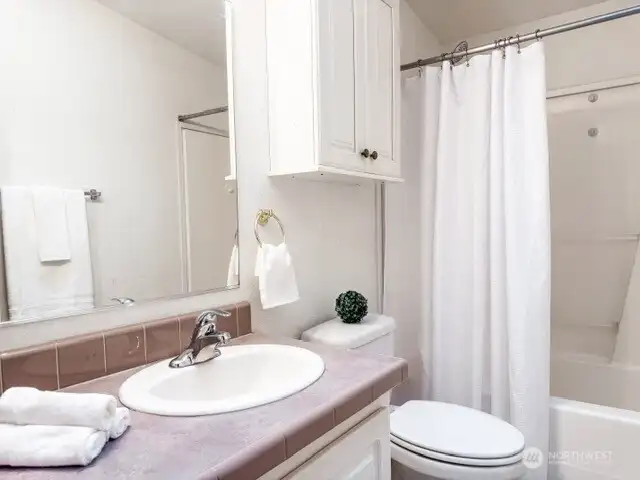 A clean, bright full bathroom equipped with a white vanity, a matching over-toilet storage cabinet, and a classic tub-and-shower combination.
