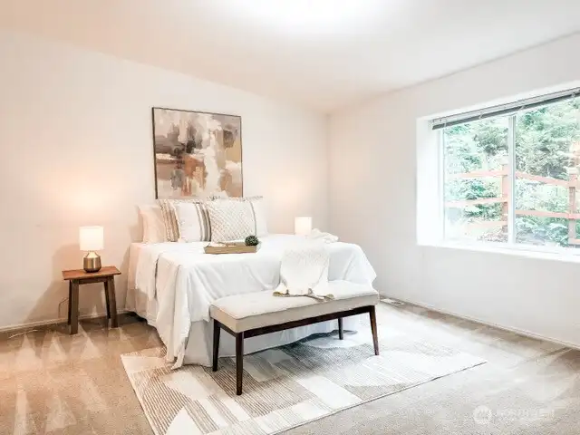 A beautifully sized, light-filled bedroom offering a peaceful retreat with plush carpeting, neutral tones, and a generous window framing the beautiful PNW greenery.
