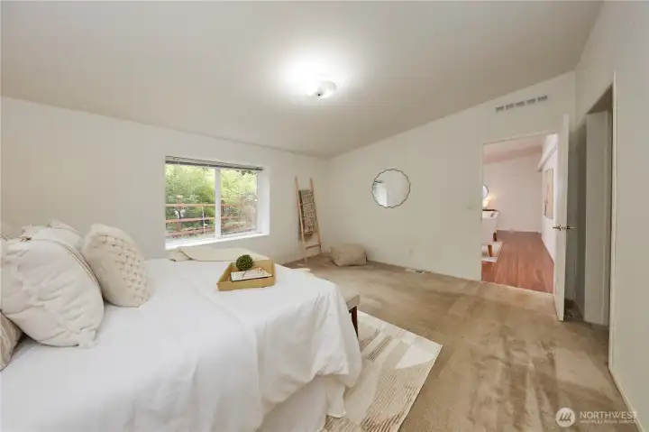 The spacious primary bedroom offers a peaceful retreat, featuring plush carpeting, generous natural light, and a large window showcasing tranquil, wooded views.