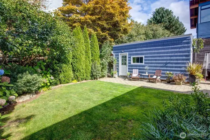 Mature landscaping in the private backyard with a crisp green lawn, paver patio, detached storage and entertaining space, and plenty of room to stretch out.