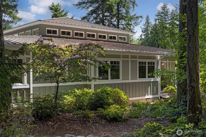 A graceful gravel approach winds through a canopy of bigleaf maples and towering firs, arriving at the home's welcoming entry façade adorned with clerestory windows and a covered front porch. The lush, naturalistic setting creates an enchanting sense of arrival befitting this private island sanctuary. A graceful gravel approach winds through a canopy of bigleaf maples and towering firs, arriving at the home's welcoming entry façade adorned with clerestory windows and a covered front porch. The lush, naturalistic setting creates an enchanting sense of arrival befitting this private island sanctuary.