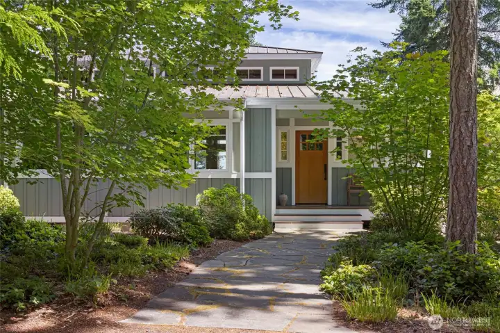 A charming flagstone pathway winds through lush vine maples and dogwoods to the covered front entry, adorned by a solid madrone tree trunk harvested from the property, creating an enchanting arrival experience that blends seamlessly with the surrounding woodland setting. A charming flagstone pathway winds through lush vine maples and dogwoods to the covered front entry, adorned by a solid madrone tree trunk harvested from the property, creating an enchanting arrival experience that blends seamlessly with the surrounding woodland setting.
