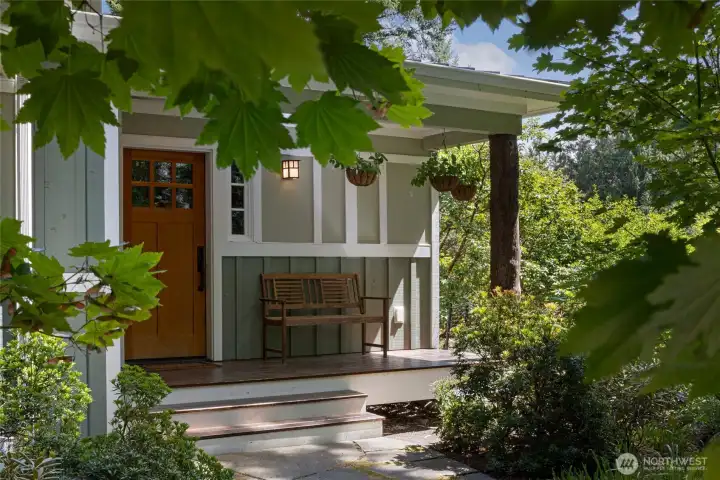 he welcoming covered front porch showcases a warm clear grain fir craftsman front door, mission-style wall lantern, hanging basket planters, and corner post constructed from a native madrona tree trunk—an inviting retreat framed by a canopy of maple trees. he welcoming covered front porch showcases a warm clear grain fir craftsman front door, mission-style wall lantern, hanging basket planters, and corner post constructed from a native madrona tree trunk—an inviting retreat framed by a canopy of maple trees.
