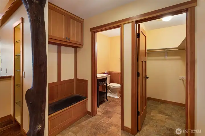 A thoughtfully designed entry features a built-in bench with overhead storage cabinets, a natural madrone tree sculptural post accent, and direct access to both a charming powder room and a spacious walk-in coat closet. Stone tile flooring and warm clear grain fir trim maintain the home's craftsman aesthetic through every functional detail. A thoughtfully designed entry features a built-in bench with overhead storage cabinets, a natural madrone tree sculptural post accent, and direct access to both a charming powder room and a spacious walk-in coat closet. Stone tile flooring and warm clear grain fir trim maintain the home's craftsman aesthetic through every functional detail.