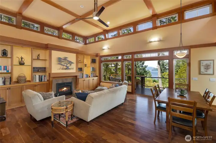 he open-concept living and dining area is bathed in natural light from an encircling band of clerestory windows above, while large picture windows and French doors frame brilliant blue water and island views just beyond the deck. The warm craftsman millwork, glowing fireplace, and hardwood floors create an inviting atmosphere that perfectly complements the stunning natural setting. he open-concept living and dining area is bathed in natural light from an encircling band of clerestory windows above, while large picture windows and French doors frame brilliant blue water and island views just beyond the deck. The warm craftsman millwork, glowing fireplace, and hardwood floors create an inviting atmosphere that perfectly complements the stunning natural setting.