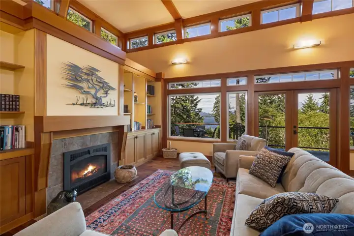 With the fire glowing warmly in the propane stone hearth, this inviting living room exudes cozy Pacific Northwest ambiance. High clerestory windows wrap the room in natural light while showcasing the surrounding evergreen canopy and shimmering water views. With the fire glowing warmly in the propane stone hearth, this inviting living room exudes cozy Pacific Northwest ambiance. High clerestory windows wrap the room in natural light while showcasing the surrounding evergreen canopy and shimmering water views.