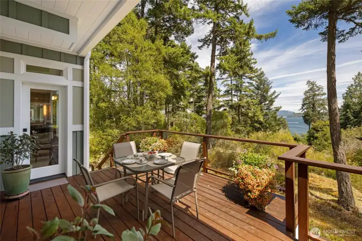 he partially covered upper deck extends seamlessly from the main living area and primary bedroom through full-height glass doors, providing a versatile outdoor dining and entertaining space with glass railings framing colorful garden plantings and panoramic water views. he partially covered upper deck extends seamlessly from the main living area and primary bedroom through full-height glass doors, providing a versatile outdoor dining and entertaining space with glass railings framing colorful garden plantings and panoramic water views.