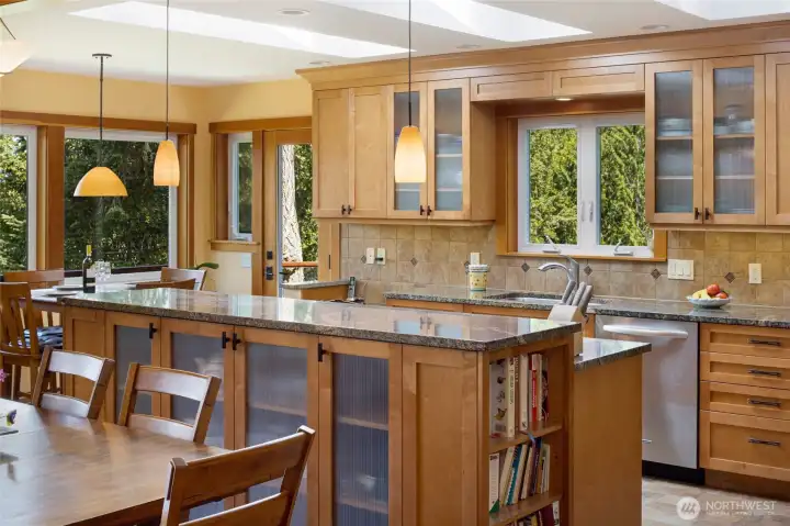 A chef's dream kitchen showcases warm fir cabinetry, dramatic granite countertops, and a generous island with built-in cookbook shelving, all bathed in natural light from bank of skylights above. Pendant lighting, glass-front uppers, and a travertine tile backsplash add refined craftsman detail throughout. A chef's dream kitchen showcases warm fir cabinetry, dramatic granite countertops, and a generous island with built-in cookbook shelving, all bathed in natural light from bank of skylights above. Pendant lighting, glass-front uppers, and a travertine tile backsplash add refined craftsman detail throughout.
