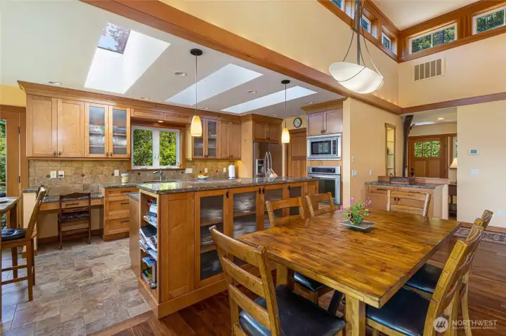 The open kitchen and dining area is flooded with natural light from large skylights, highlighting the honey-toned cabinetry, granite island, and stainless appliances against a backdrop of clerestory windows. The spacious layout easily accommodates a large dining table, making it ideal for entertaining. The open kitchen and dining area is flooded with natural light from large skylights, highlighting the honey-toned cabinetry, granite island, and stainless appliances against a backdrop of clerestory windows. The spacious layout easily accommodates a large dining table, making it ideal for entertaining.