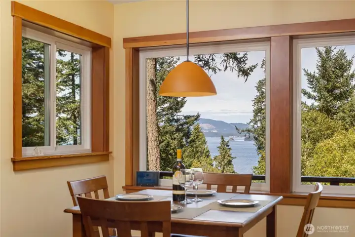 This sun-drenched breakfast nook offers an intimate dining experience framed by large wood-trimmed windows that capture breathtaking views of the water, islands, and evergreen forest beyond. A warm amber pendant light and richly grained wood table complete this inviting everyday retreat. This sun-drenched breakfast nook offers an intimate dining experience framed by large wood-trimmed windows that capture breathtaking views of the water, islands, and evergreen forest beyond. A warm amber pendant light and richly grained wood table complete this inviting everyday retreat.
