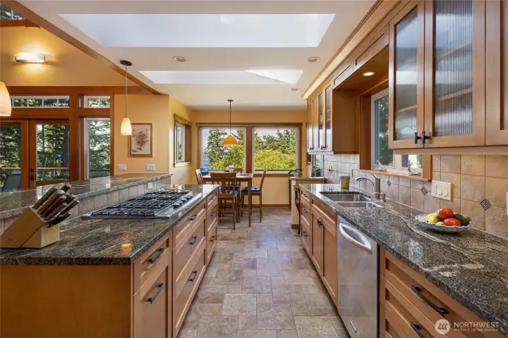 The galley-style kitchen corridor offers ample prep space along dual granite countertops, with a stainless undermount sink, integrated dishwasher, and a travertine tile backsplash on one side and the cooktop island on the other. Views through the nook window frame the water and coastal landscape, making even daily tasks a pleasure. The galley-style kitchen corridor offers ample prep space along dual granite countertops, with a stainless undermount sink, integrated dishwasher, and a travertine tile backsplash on one side and the cooktop island on the other. Views through the nook window frame the water and coastal landscape, making even daily tasks a pleasure.