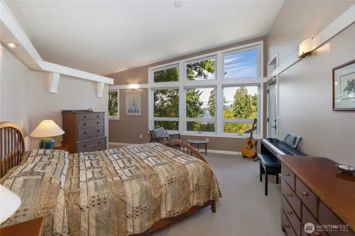 he expansive primary suite boasts soaring vaulted ceilings and dramatic floor-to-ceiling windows that frame breathtaking treetop and water views, bathing the room in natural light. An all glass exterior door adds a seamless transition to the viewing deck. he expansive primary suite boasts soaring vaulted ceilings and dramatic floor-to-ceiling windows that frame breathtaking treetop and water views, bathing the room in natural light. An all glass exterior door adds a seamless transition to the viewing deck.
