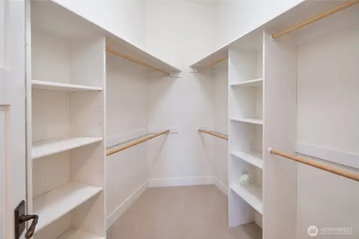 The spacious walk-in closet features custom white built-in shelving, double hanging rods, and ample adjustable storage on all sides, offering exceptional organization for even the most extensive wardrobe. Plush carpeting and clean lines create a boutique-style dressing experience. The spacious walk-in closet features custom white built-in shelving, double hanging rods, and ample adjustable storage on all sides, offering exceptional organization for even the most extensive wardrobe. Plush carpeting and clean lines create a boutique-style dressing experience.
