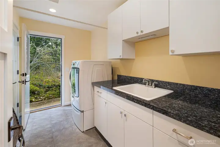 Generously sized laundry room is appointed with white shaker cabinetry, blue pearl granite counters, a utility sink, and a front-loading washer and dryer, all with direct exterior access from the landscaped grounds. The thoughtful layout provides ample workspace and storage for a fully functional utility area. Generously sized laundry room is appointed with white shaker cabinetry, blue pearl granite counters, a utility sink, and a front-loading washer and dryer, all with direct exterior access from the landscaped grounds. The thoughtful layout provides ample workspace and storage for a fully functional utility area.