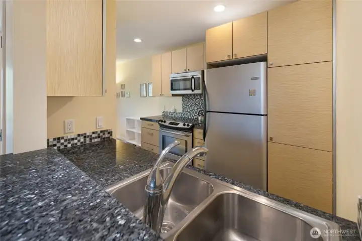 Efficiently designed guest quarters kitchen features sleek light maple cabinetry, bold granite countertops, and a full suite of stainless steel appliances including a French door refrigerator, electric range, and over-the-range microwave. A mosaic tile backsplash adds a sophisticated finishing touch to this functional culinary space. Efficiently designed guest quarters kitchen features sleek light maple cabinetry, bold granite countertops, and a full suite of stainless steel appliances including a French door refrigerator, electric range, and over-the-range microwave. A mosaic tile backsplash adds a sophisticated finishing touch to this functional culinary space.