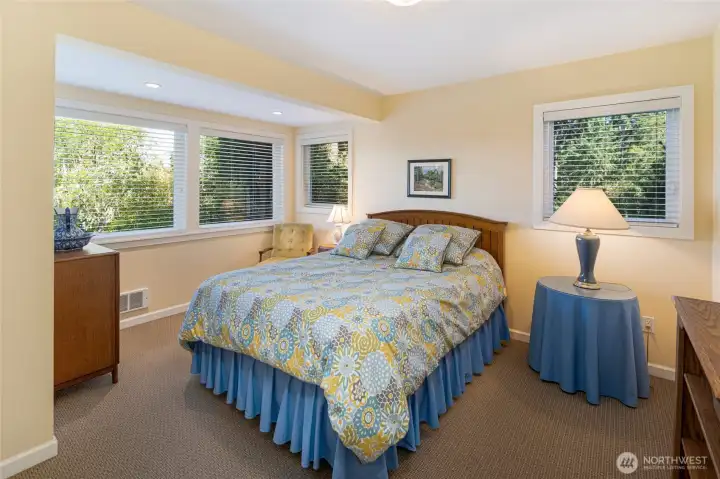 Spacious guest bedroom is bathed in natural light through large windows overlooking water views and mature tree canopy, creating a serene woodland retreat. Spacious guest bedroom is bathed in natural light through large windows overlooking water views and mature tree canopy, creating a serene woodland retreat.