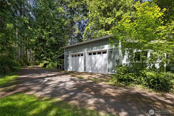 An oversized detached two-car garage and carport finished in matching sage board-and-batten siding with white carriage-style doors offers ample storage and parking, accessed by a generous gravel driveway winding through mature trees. The structure's thoughtful design complements the main residence while adding exceptional practicality to the property. An oversized detached two-car garage and carport finished in matching sage board-and-batten siding with white carriage-style doors offers ample storage and parking, accessed by a generous gravel driveway winding through mature trees. The structure's thoughtful design complements the main residence while adding exceptional practicality to the property.