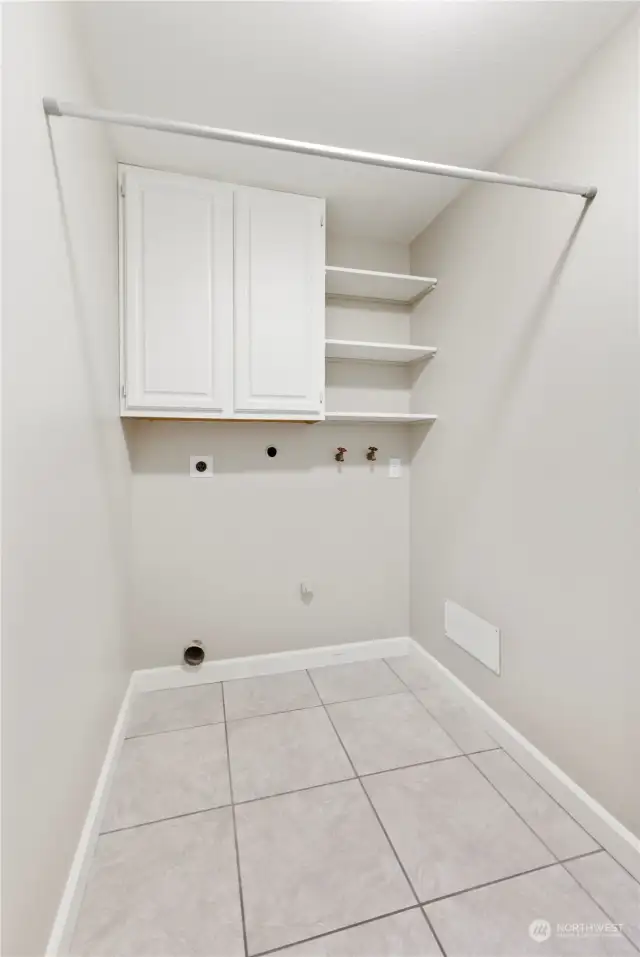 Lower level Laundry area has cabinets on both sides of room, tiled floors and clothes hanging bar