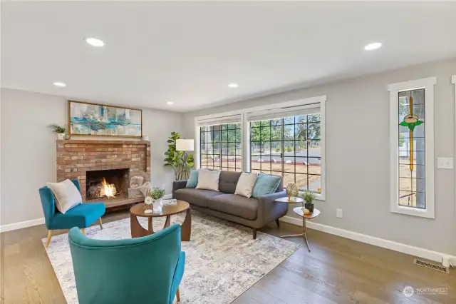 Living room has big open windows, wood fireplace & lots of natural light. Stain glass accent window next to front door adds a whimsical touch to the space