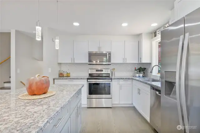 Kitchen has a modern flare with white main cabinets, pendant lighting, custom tiled backsplash & newer stainless steel appliances