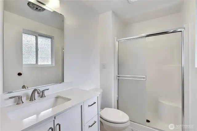 Fresh and modern primary bathroom featuring a sleek white vanity with quartz countertop, brushed nickel fixtures, and an oversized mirror for a bright, polished feel. The step-in shower with sliding glass doors offers ease and functionality, completing this well-appointed private space.