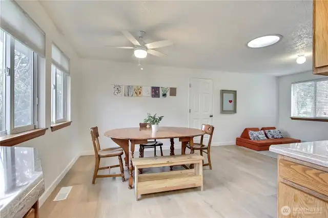 Bright and inviting dining area showcases brand new wide-plank flooring, a sleek modern ceiling fan, and abundant natural light streaming through a wall of windows. Seamlessly connected to the family room, this space is perfect for both casual meals and lively gatherings—blending comfort and functionality with effortless style.