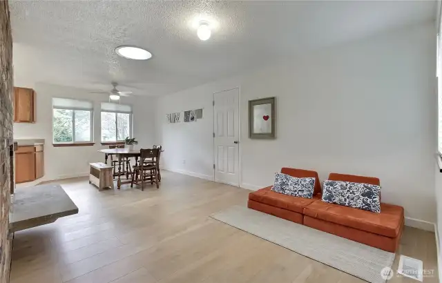 Expanded view of the dining and family room highlights the home's open layout and stylish wide-plank flooring throughout. The flexible floorplan allows for multiple functional zones—dining, lounging, or play—while maintaining a clean and cohesive aesthetic.
