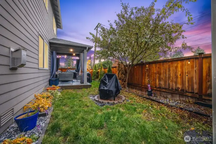 Fully fenced backyard with mature trees, fire pit and patio access.