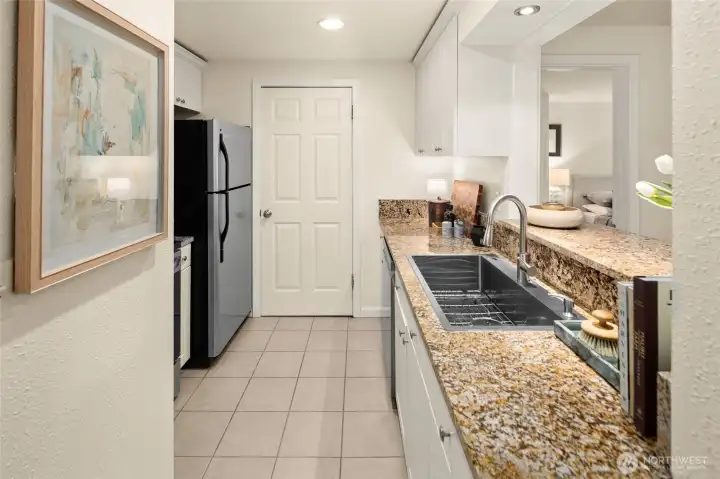 Streamlined galley kitchen with fantastic, functional layout - featuring new stove, dishwasher, microwave, and sink (all updated September 2025). The door straight ahead leads to the in-unit washer and dryer for added everyday convenience.